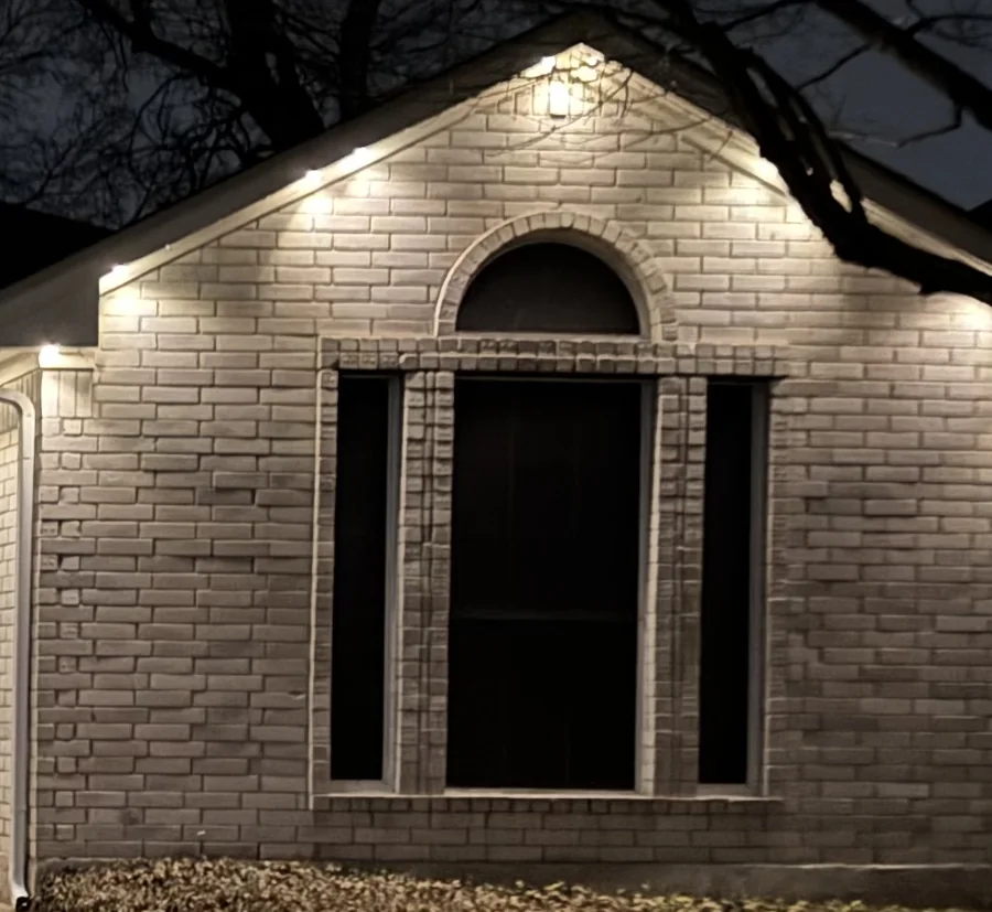 A Gemstone gable with a bright cone of light under each light and darker scallops between them on the brick