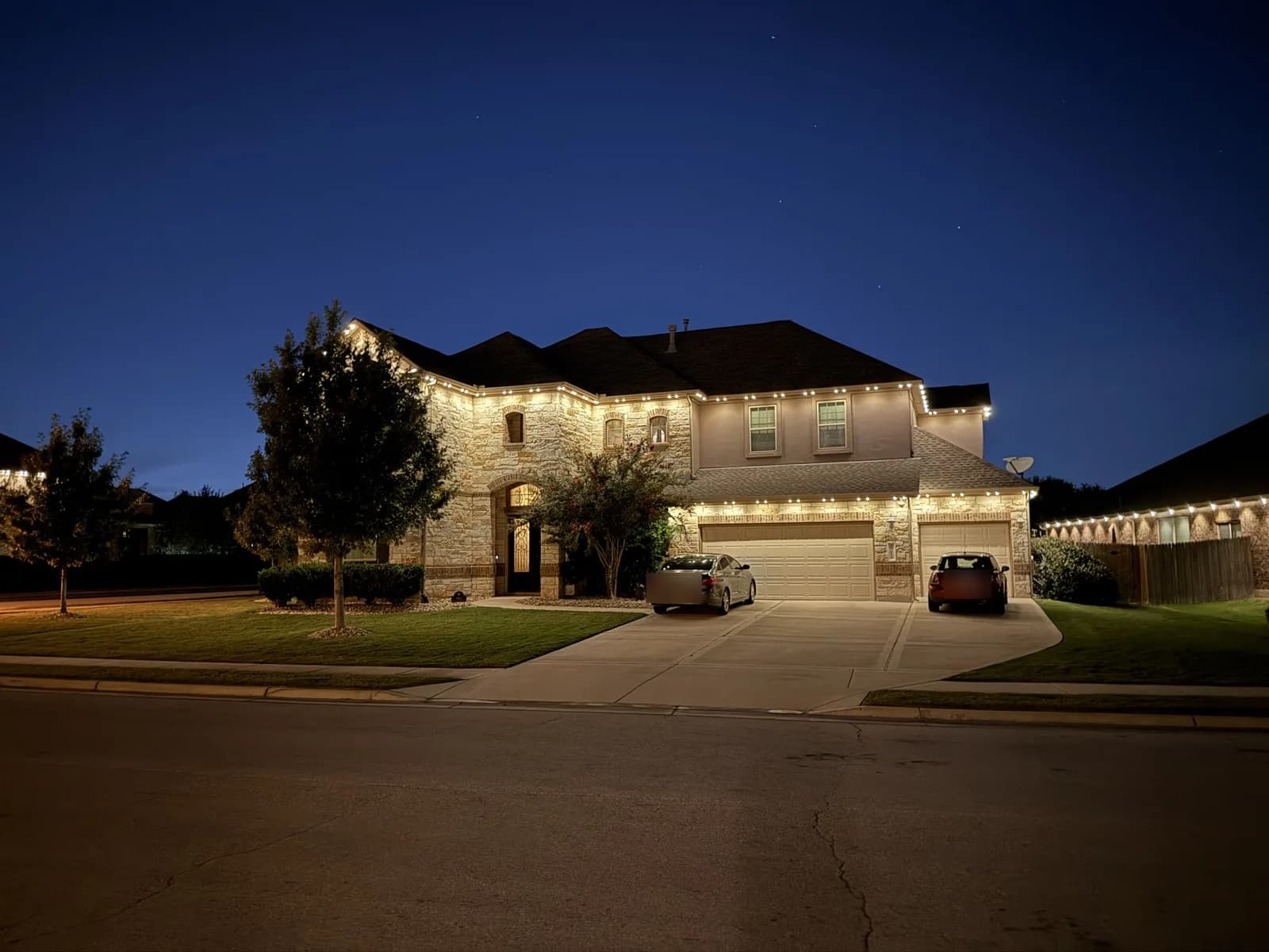 A TruLight home in warm white at dusk, with a neighboring home's protruding-lens lights visible at the right edge