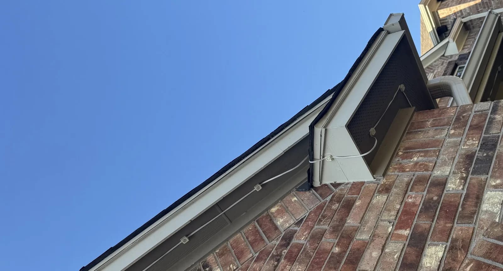 Govee cable crossing an open gap at a roofline corner in daylight, with pucks attached to the trim