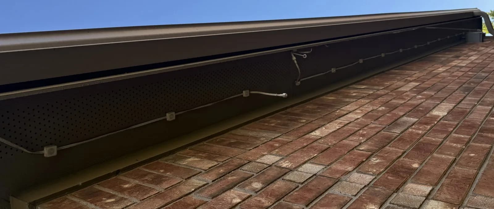 Govee cable and pucks stuck to a perforated soffit in daylight, with a loose connector hanging between two runs