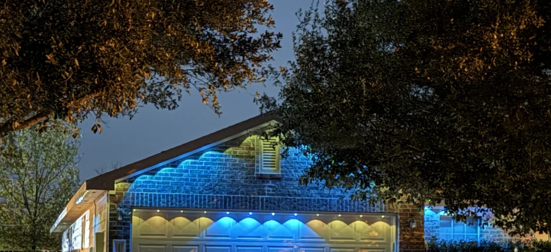 Govee permanent outdoor lights creating distinct pools of blue and warm-white light across a garage fascia