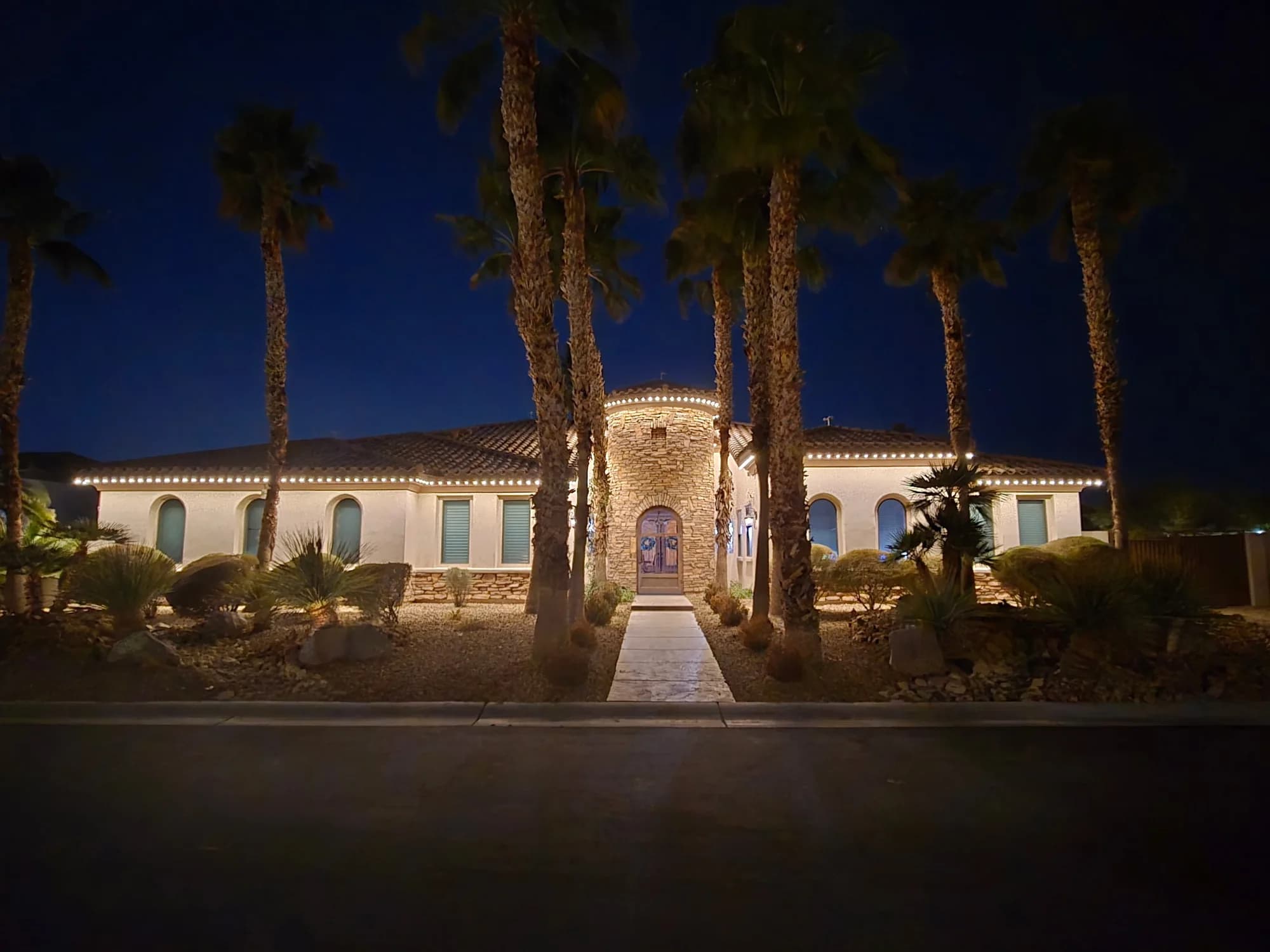 Warm-white TruLight lighting around a stucco home with a round stone entry and tall palms.