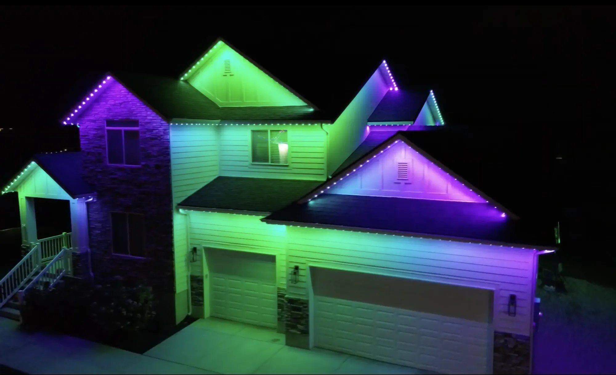 Aerial night view of a two-story TruLight home with purple and green roofline lighting.
