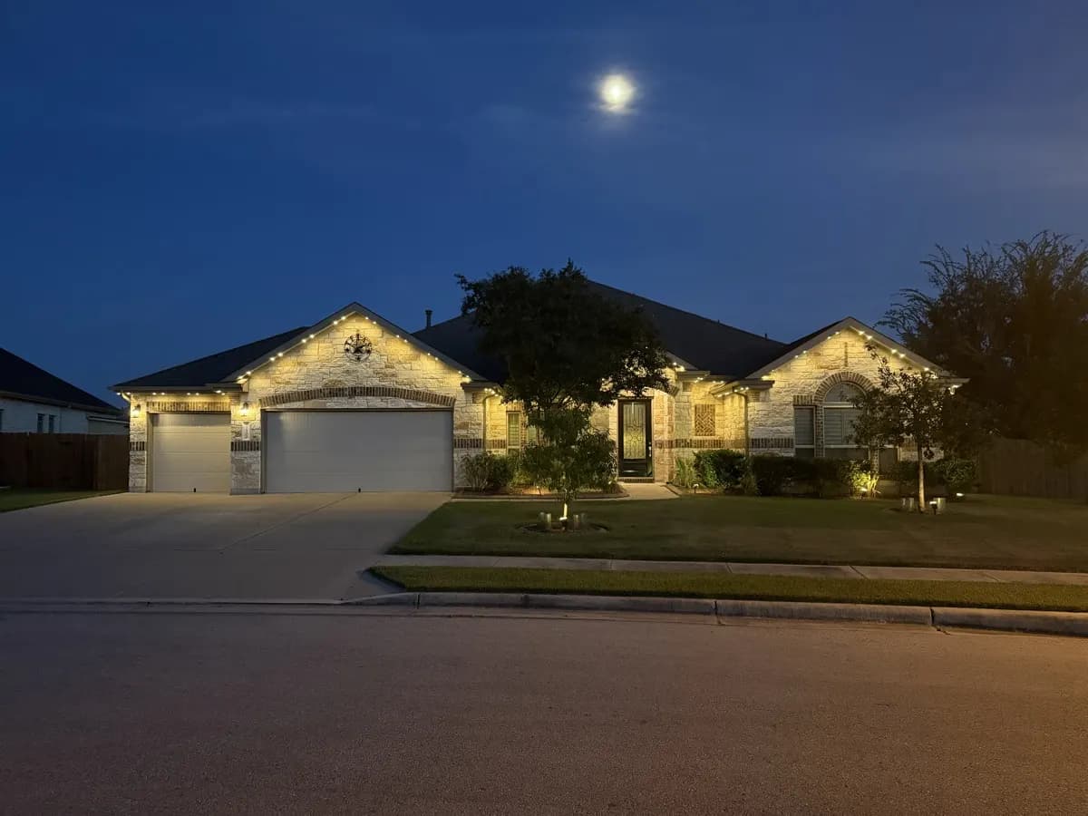 Warm-white TruLight roofline lighting on a single-story ranch home at dusk under a full moon.