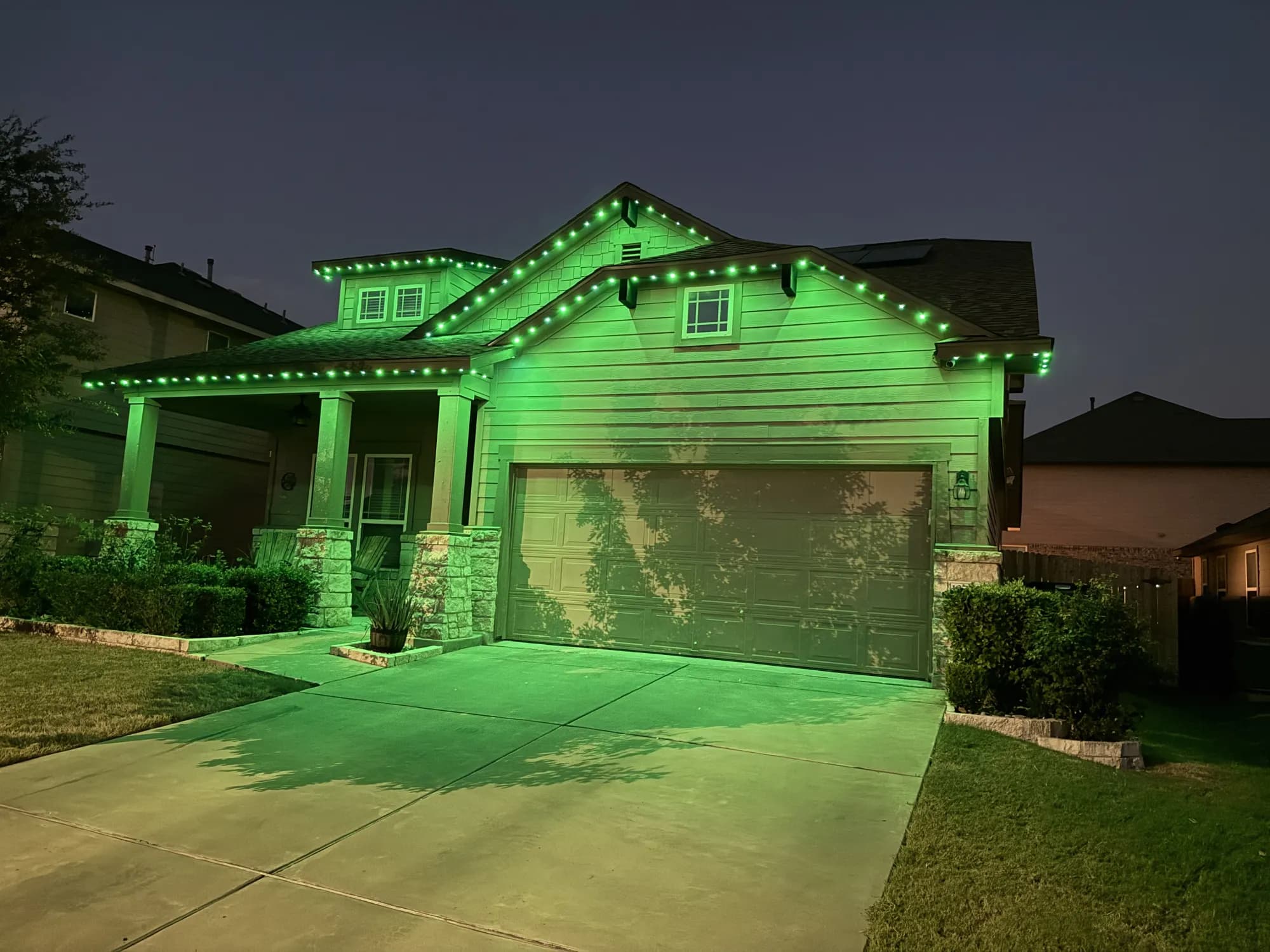 Green TruLight roofline lighting on a home with siding and stone porch columns at night.