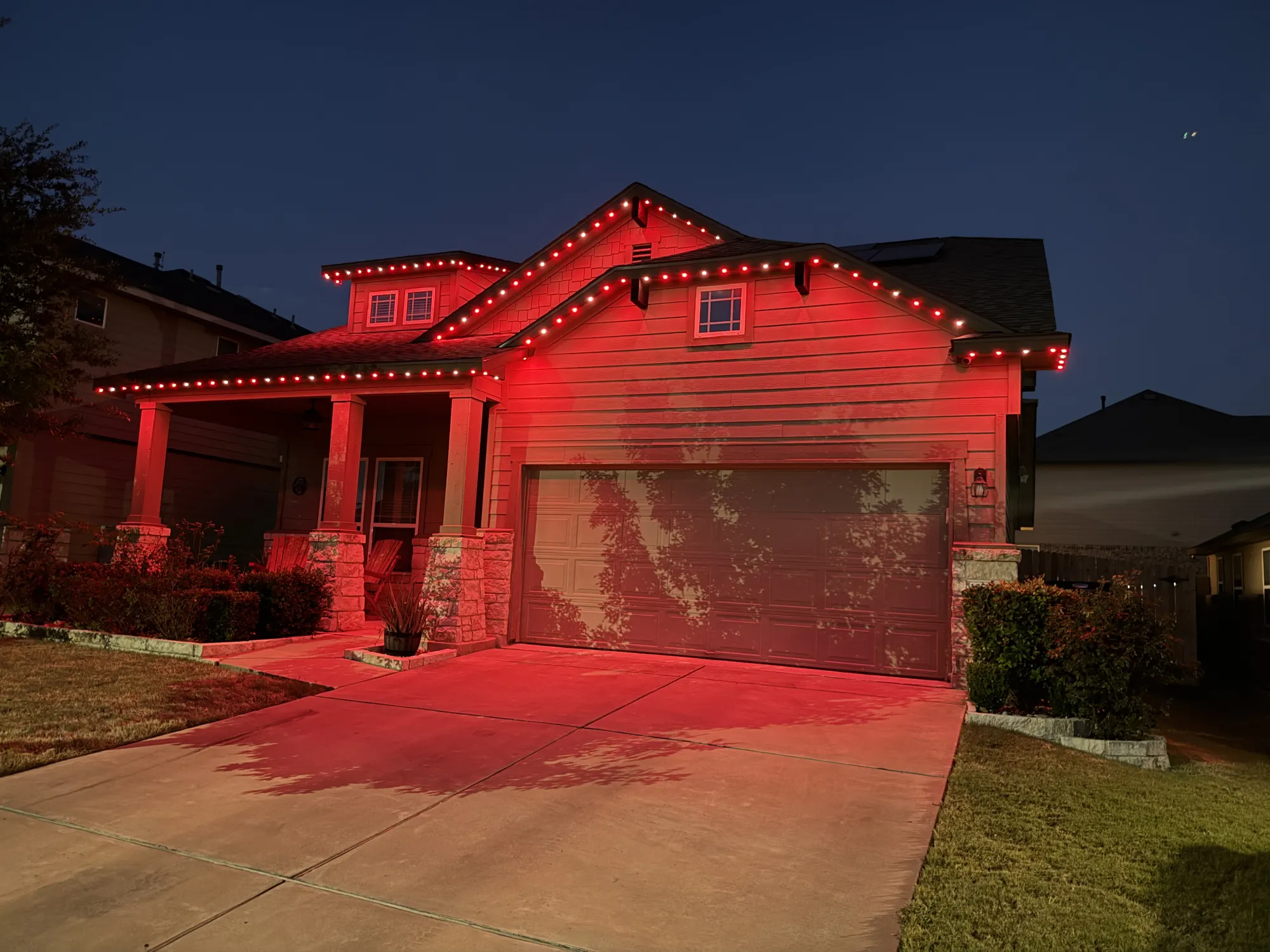Red TruLight roofline lighting on a home with siding and stone porch columns at night.