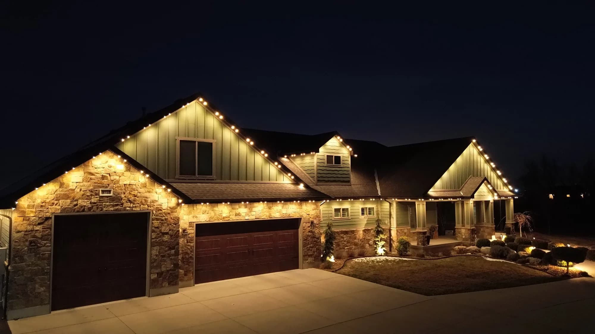 Warm-white TruLight roofline lighting across a stone home and its front entry.
