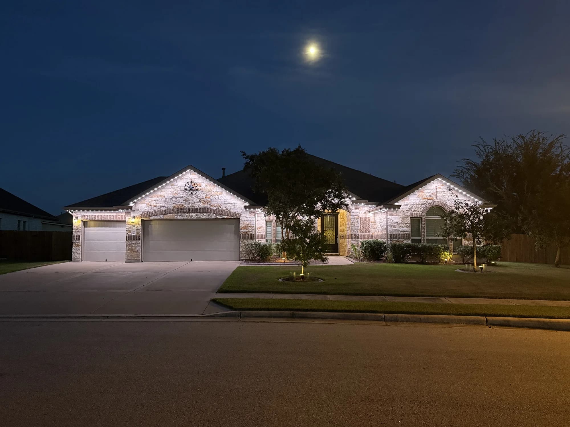 White TruLight roofline lighting on a Texas home beneath a moonlit sky.