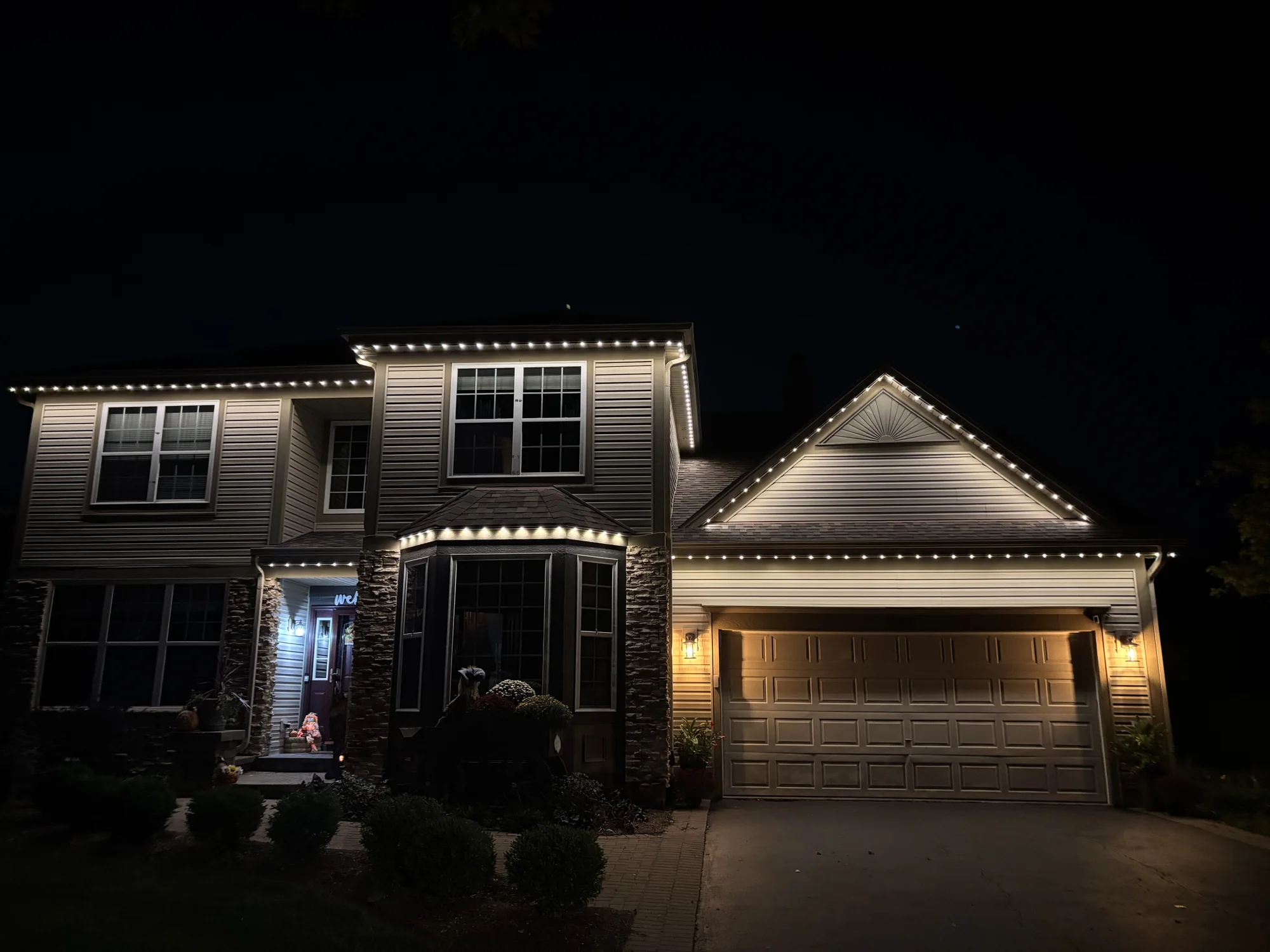 White TruLight lighting outlining a two-story home and its garage after dark.