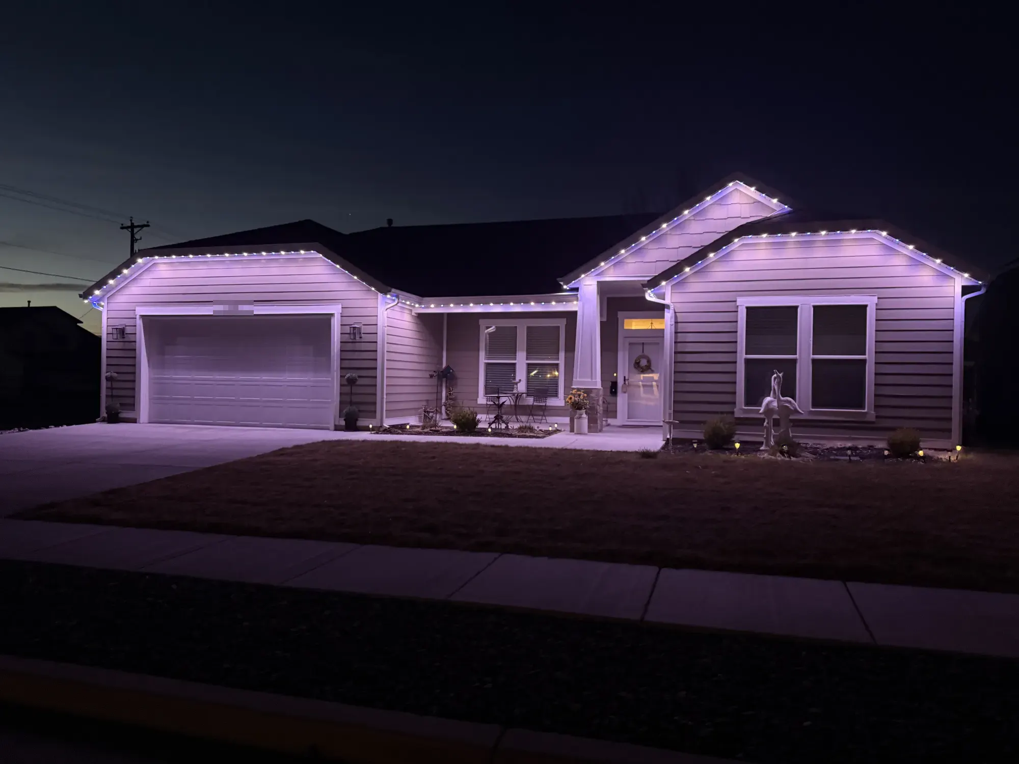 Lavender TruLight roofline lighting on a single-story home with gray siding at night.