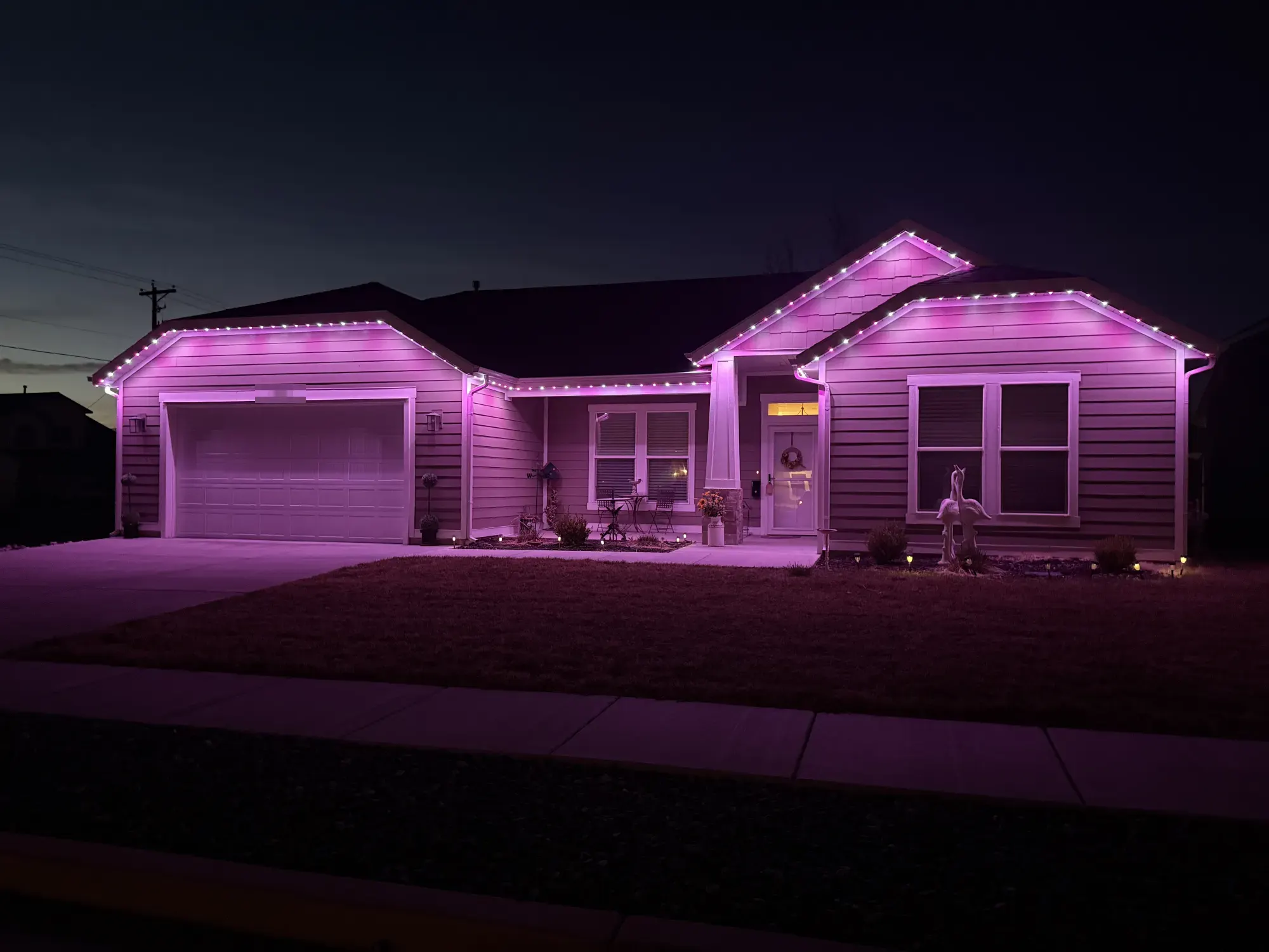 Pink and purple TruLight roofline lighting on a single-story home with gray siding at night.