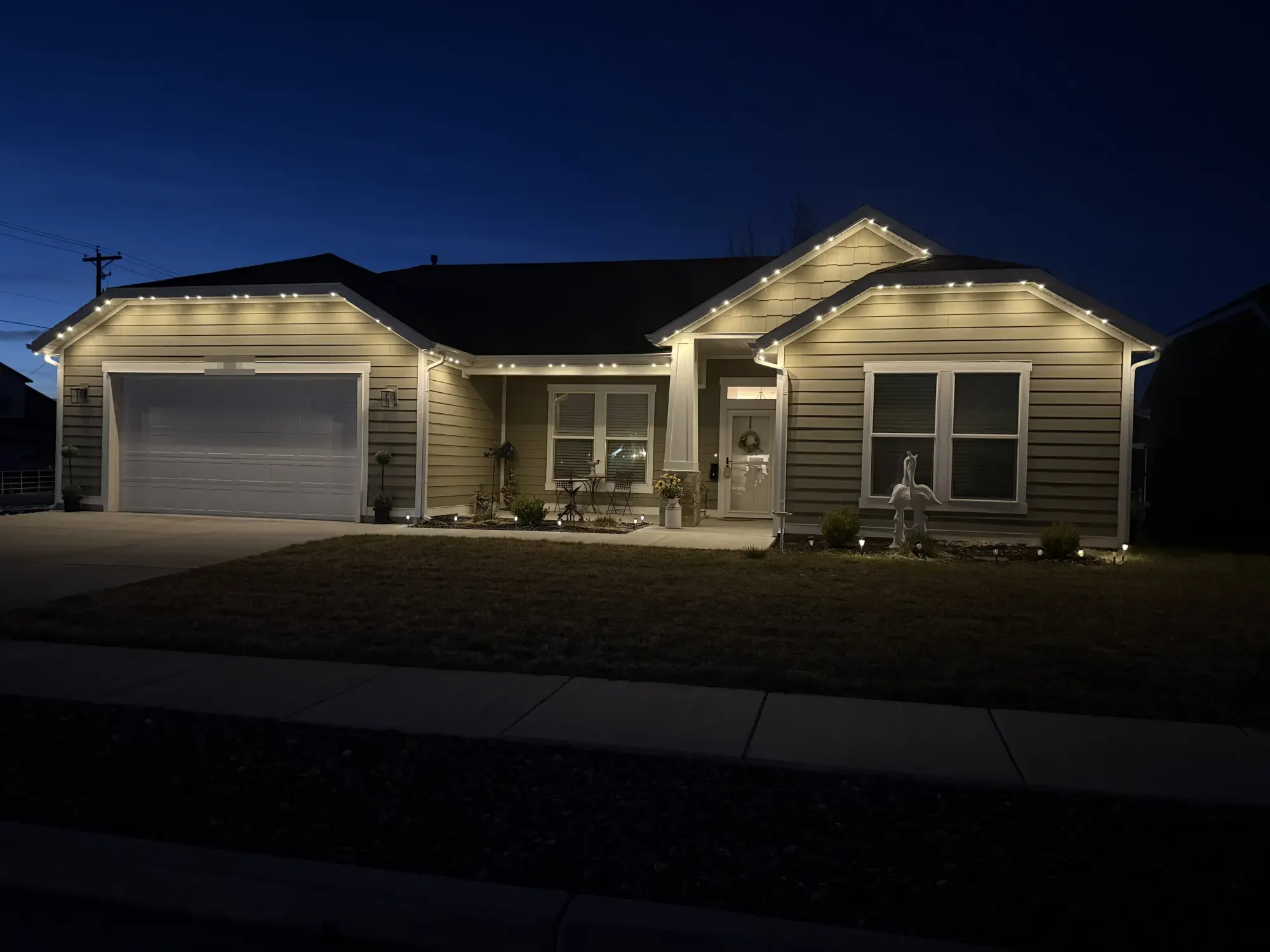 Warm-white TruLight roofline lighting on a single-story home with gray siding at dusk.