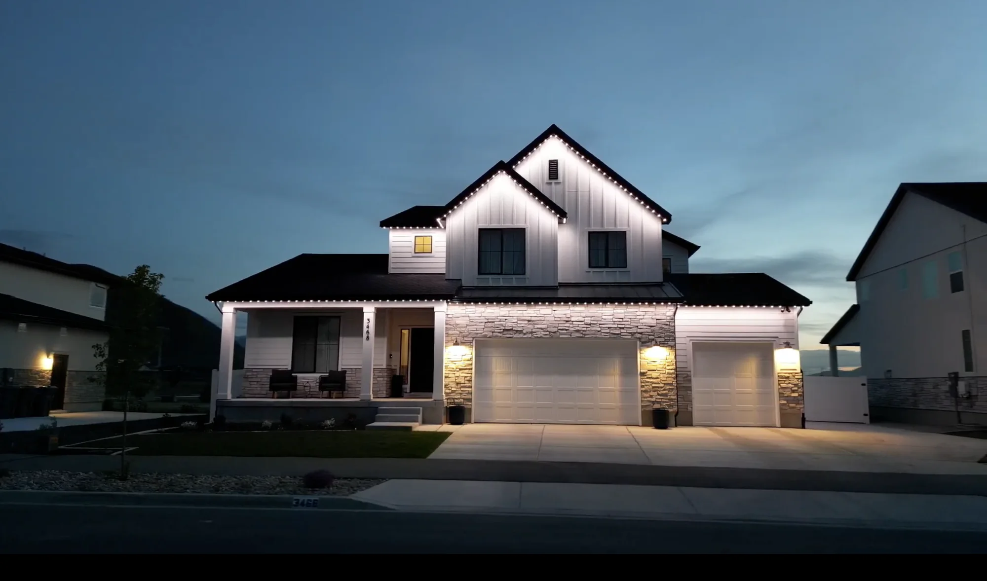 White TruLight roofline lighting on a two-story farmhouse with stone porch columns.